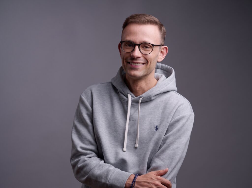 Darius Krutzek im grauen Kapuzenpullover vor grauem Hintergrund